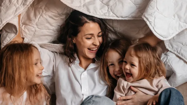 Happy mother with three girls holding blanket on sofa at home