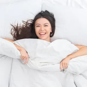 Young brunette woman on bed top view looking camera laughing cheerful