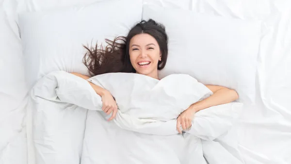 Young brunette woman on bed top view looking camera laughing cheerful