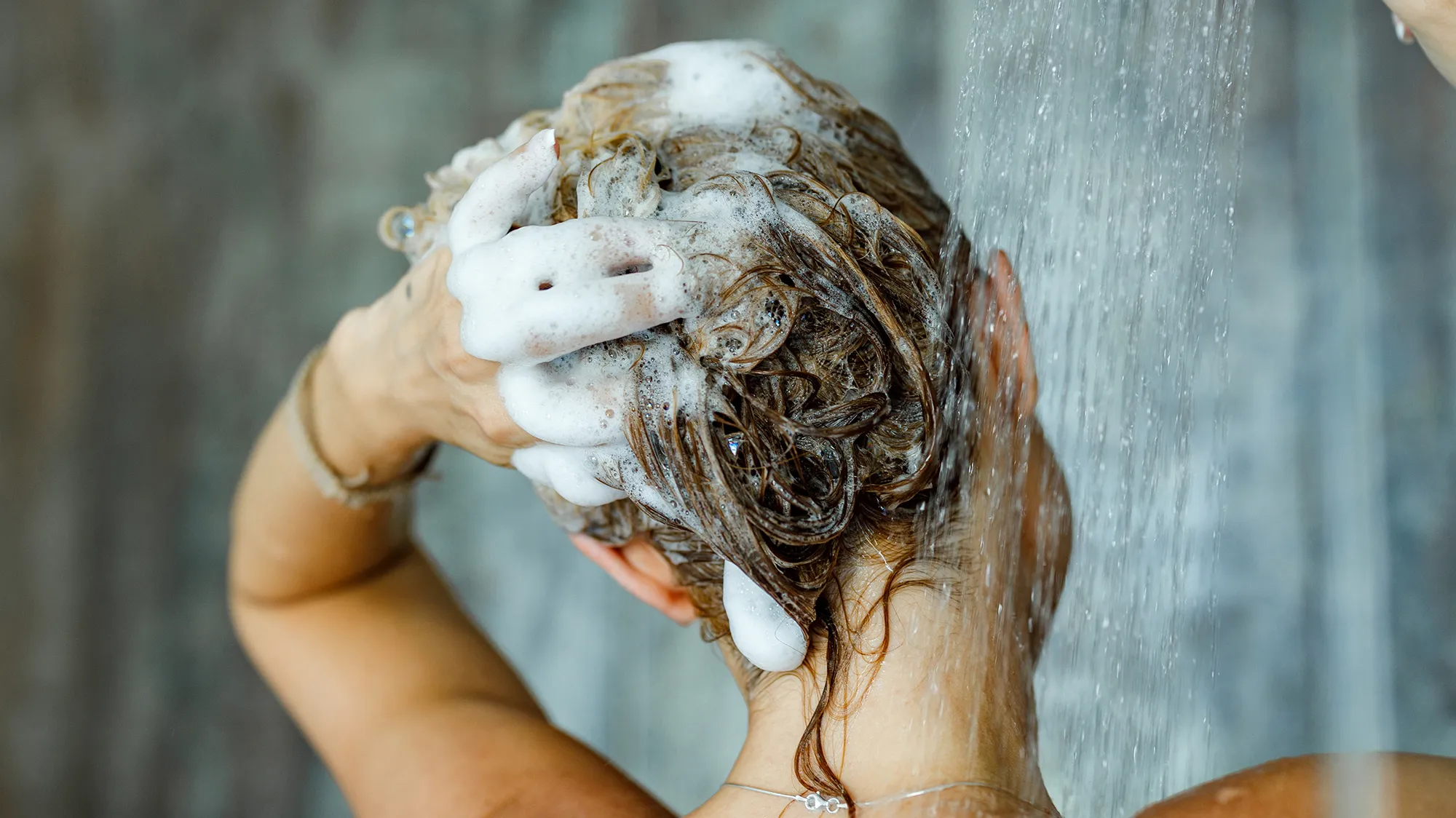 Back view of a woman washing her hair with a shampoo in bathroom. Copy space.