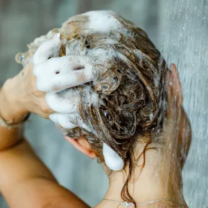 Back view of a woman washing her hair with a shampoo in bathroom. Copy space.