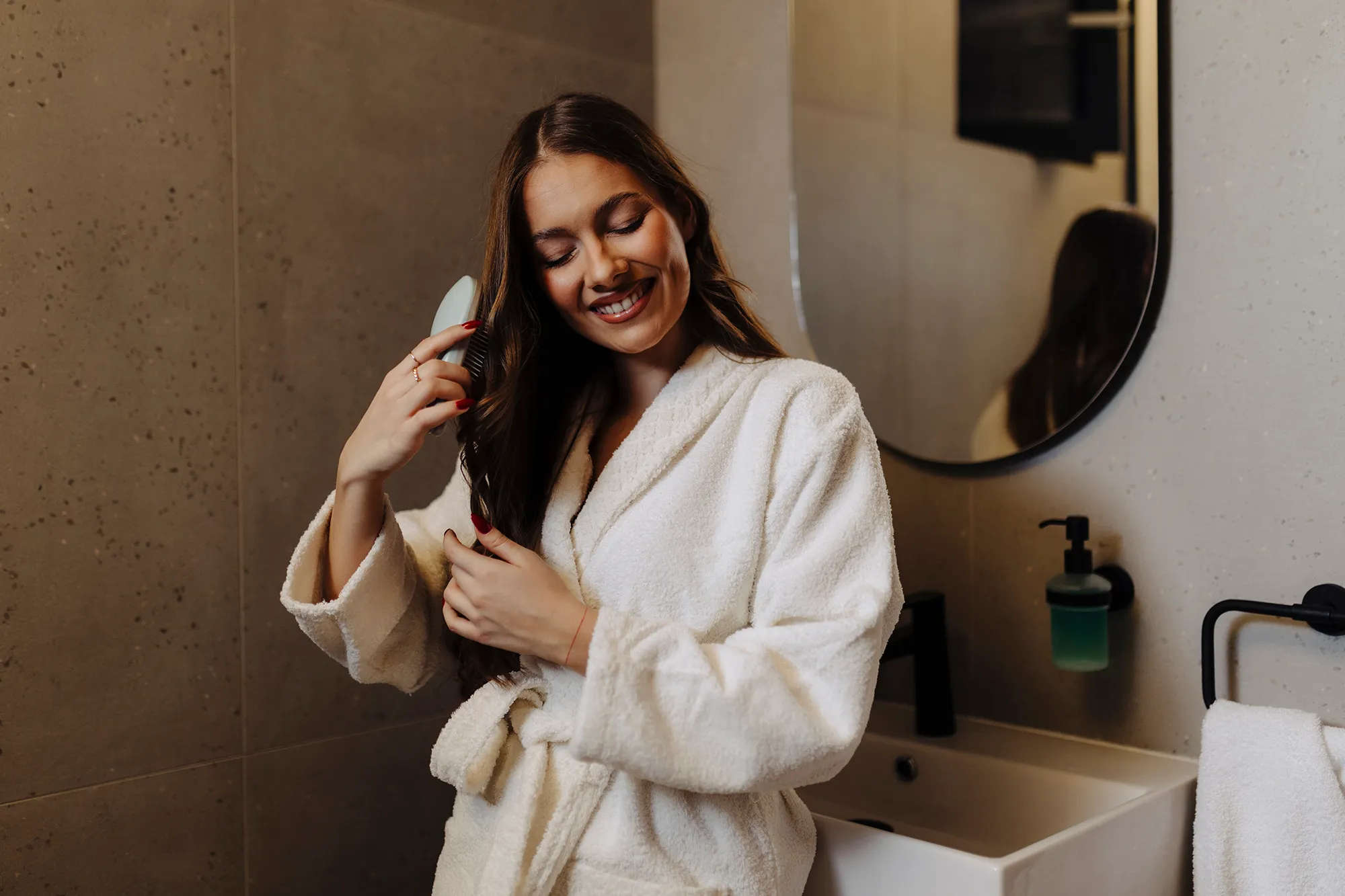Woman Combing Her Beautiful Hair With Brush While Standing Near Mirror In Bathroom