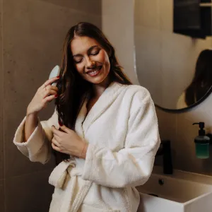 Woman Combing Her Beautiful Hair With Brush While Standing Near Mirror In Bathroom