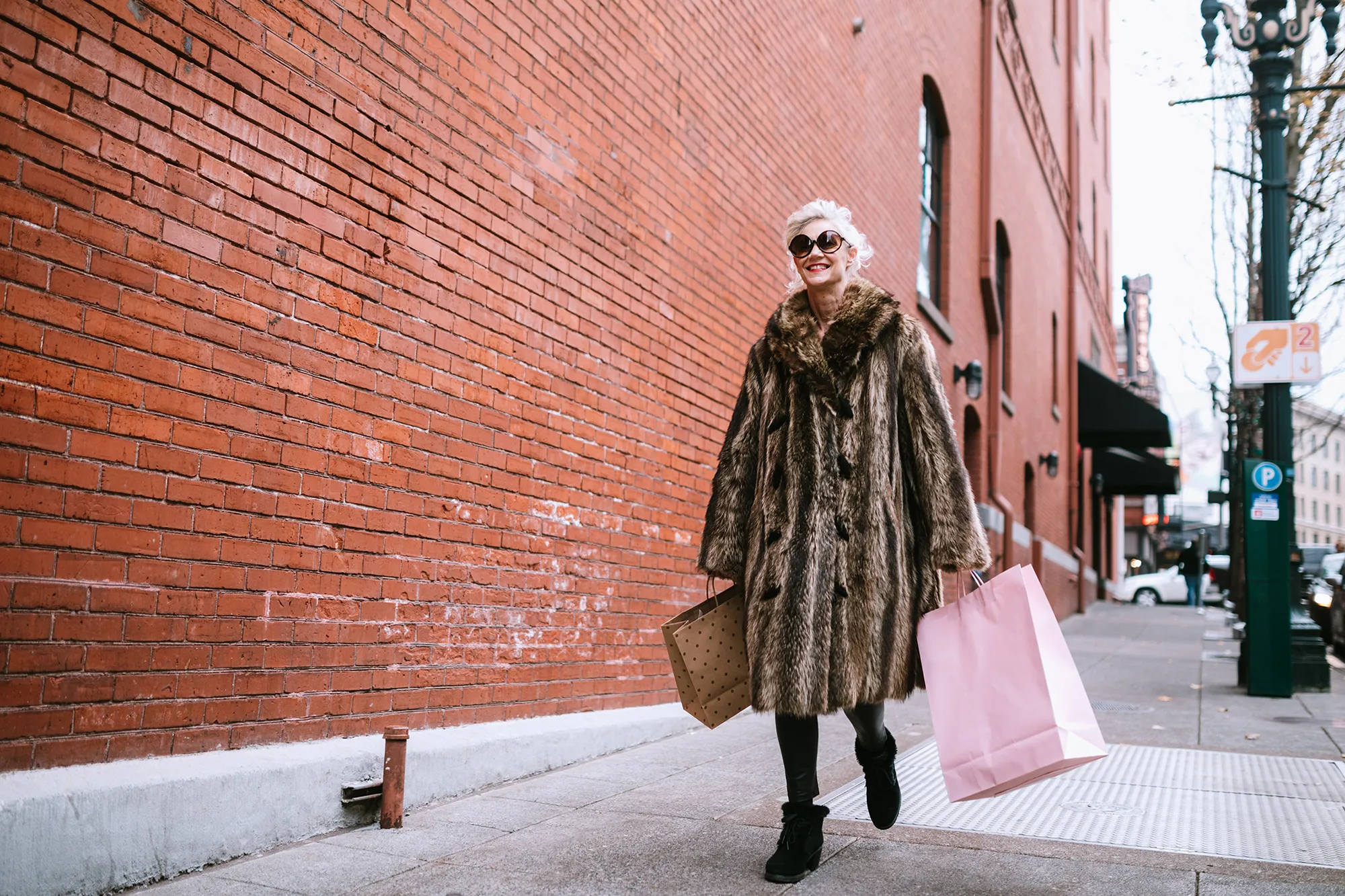 A fun and cheerful senior woman enjoys a day out shopping on the town in the city of Portland, Oregon. She wears fashionable clothing with a bit of flair and playfulness, carrying her bags of purchased gifts in her hands.