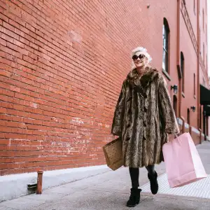 A fun and cheerful senior woman enjoys a day out shopping on the town in the city of Portland, Oregon. She wears fashionable clothing with a bit of flair and playfulness, carrying her bags of purchased gifts in her hands.