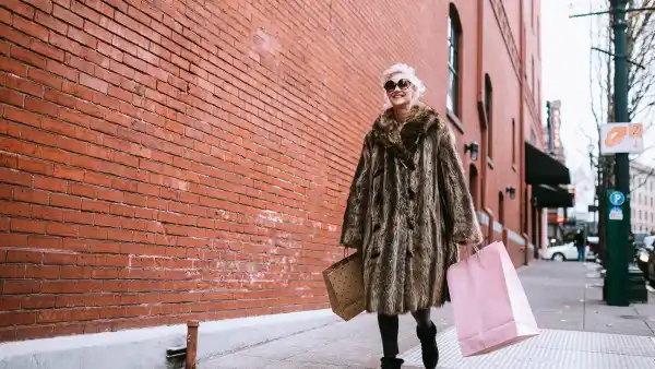 A fun and cheerful senior woman enjoys a day out shopping on the town in the city of Portland, Oregon. She wears fashionable clothing with a bit of flair and playfulness, carrying her bags of purchased gifts in her hands.