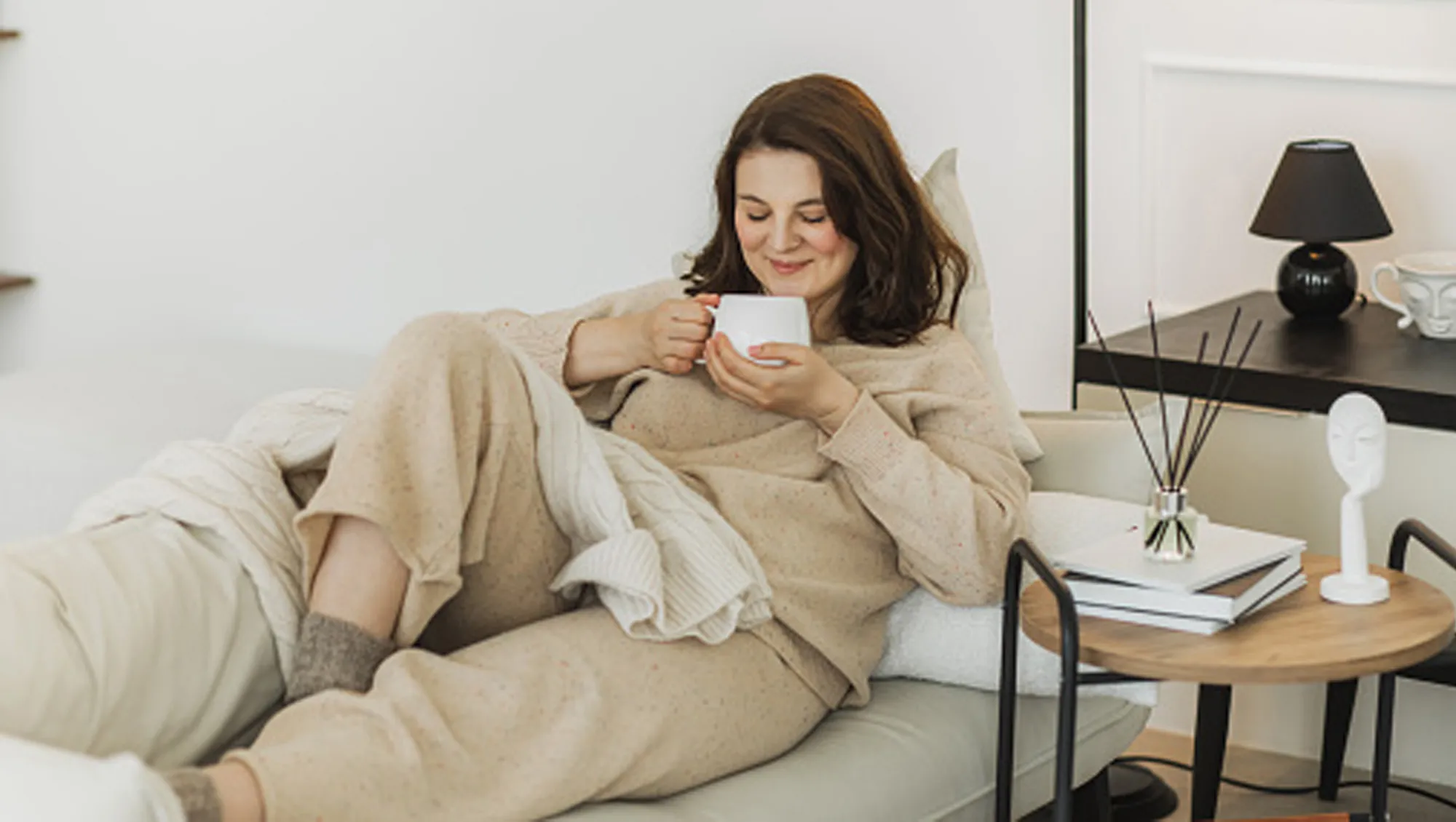 woman wearing beige loungewear set sipping a cup of tea