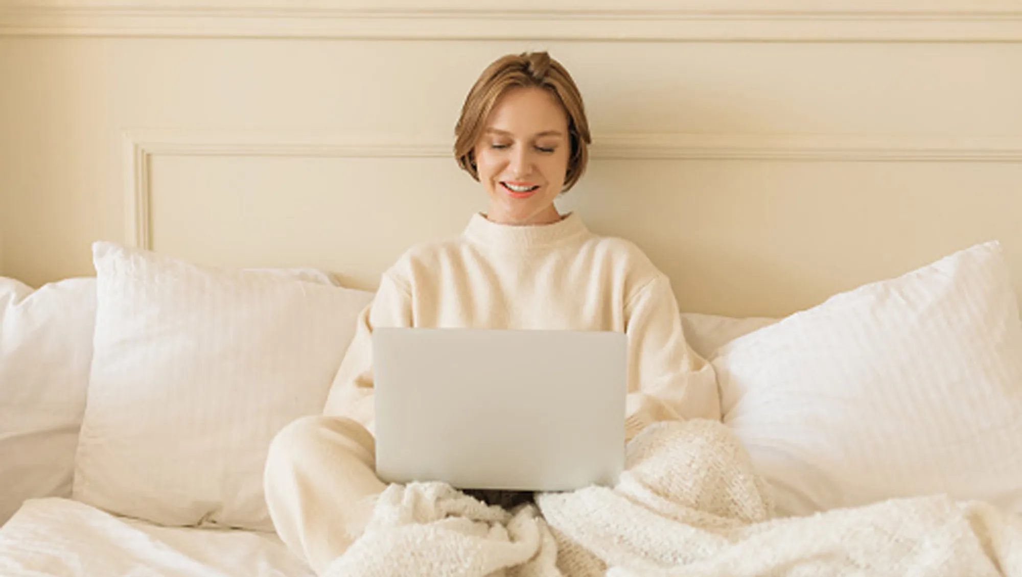 woman in bed on laptop in cream loungewear