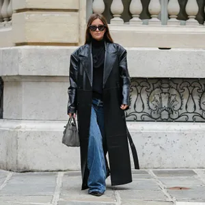 Diane Batoukina wears black Saint Laurent sunglasses, a black Tods turtleneck, a black faux leather long The Frankie Shop trench coat, a grey leather Birkin Hermes bag, blue denim jeans / pants, black leather Bershka shoes, during a street style fashion photo session, on October 18, 2024 in Paris, France.