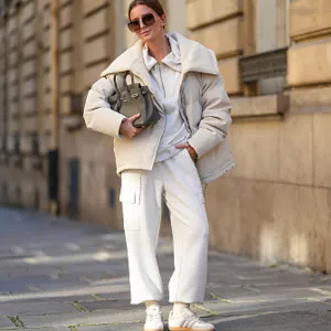 Diane Batoukina wears black Dior sunglasses, a white Varley puffer jacket, a white Adidas sweatshirt, white Varley pants, a grey leather Birkin Hermes bag, white socks, white Samba Adidas sneakers shoes, during a street style fashion photo session, on October 23, 2024 in Paris, France.