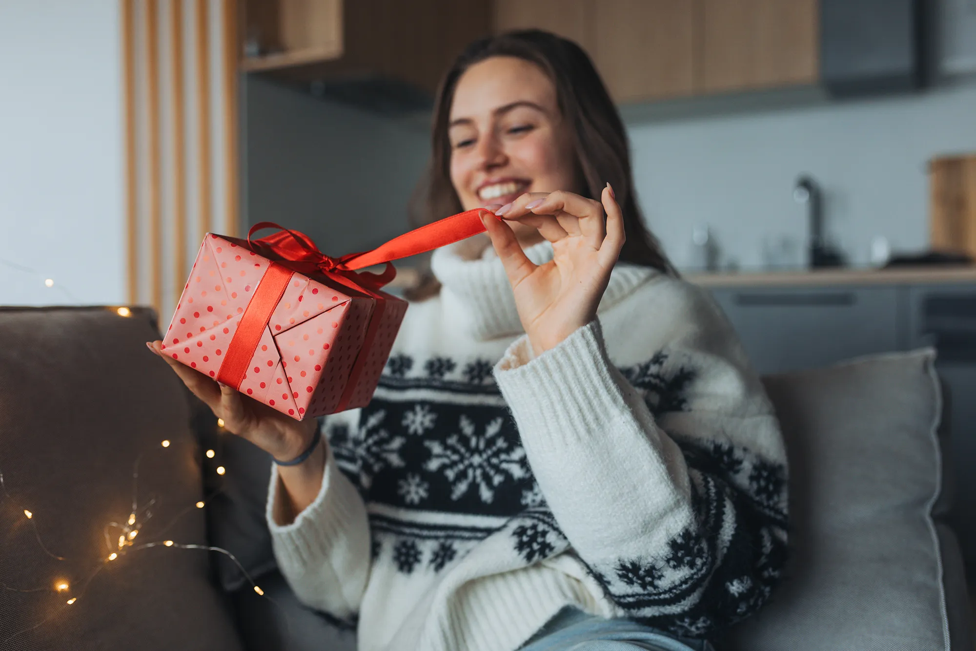 Beautiful woman holding a wrapped gift in her hand, opening it and smiling. A Christmas surprise or birthday gift from a friend delivered by mail.