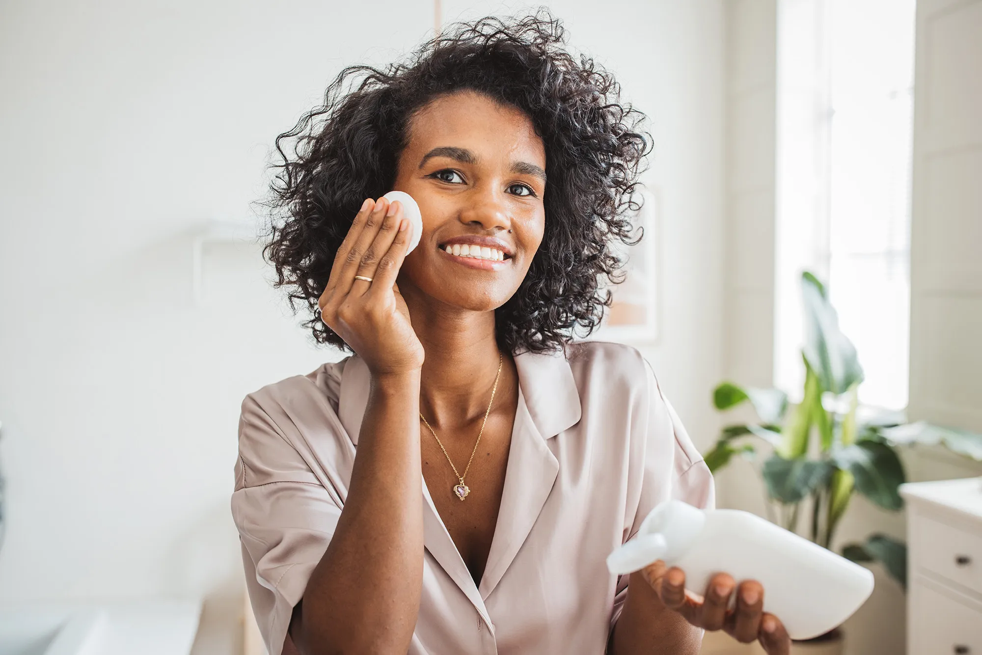 Young woman in bathroom applying moisturizing cream on her skin after having a bath.