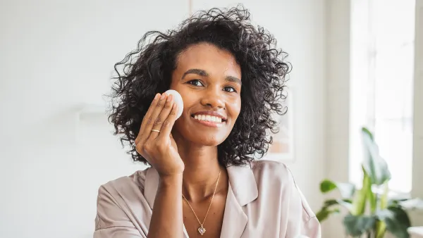 Young woman in bathroom applying moisturizing cream on her skin after having a bath.