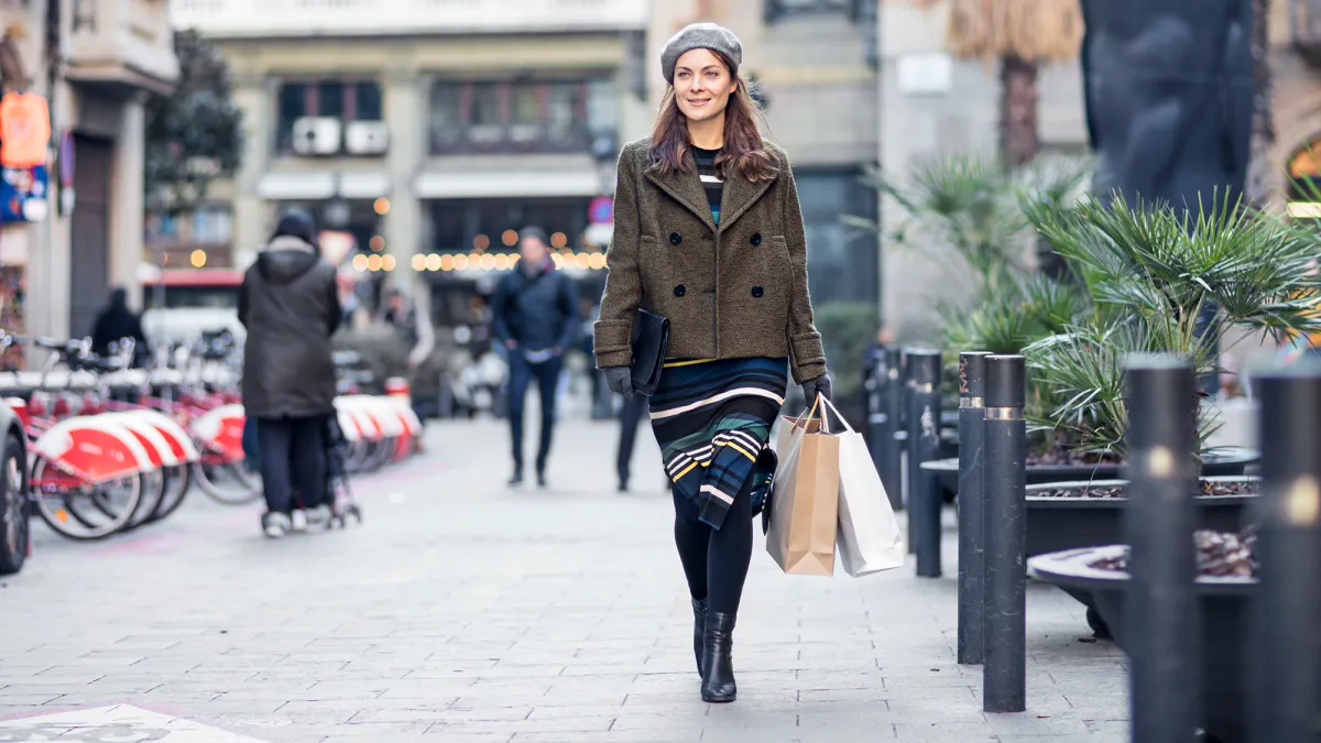 Full length of woman looking away while walking on footpath. Thoughtful female is carrying shopping bags in city. She is in warm clothing.