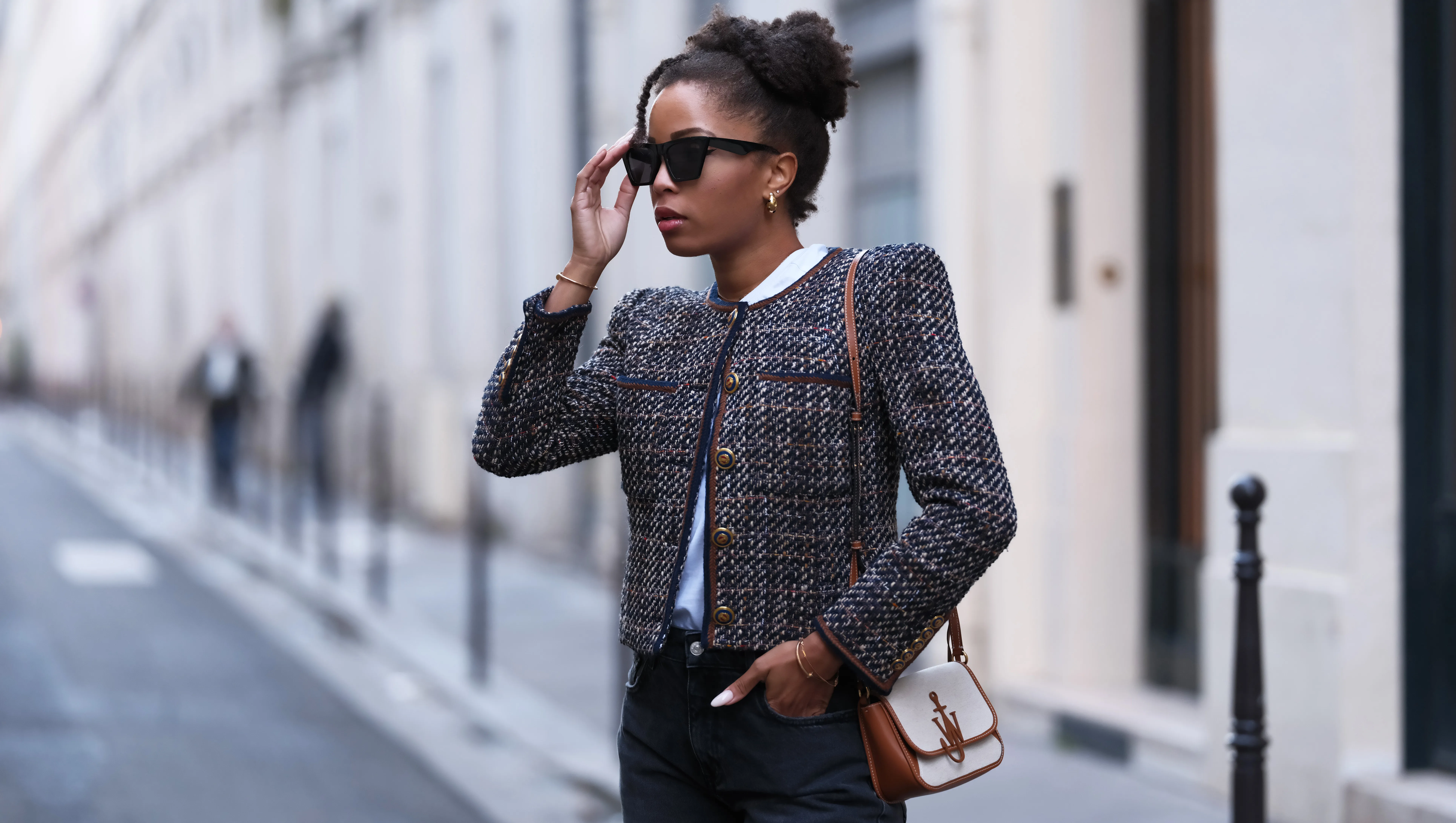 PARIS, FRANCE - NOVEMBER 06: Ellie Delphine wears sunglasses, a white t-shirt, a tweed jacket with bronze buttons from Veronica Beard, flared denim / jeans pants from Zara, a brown and white JW Anderson bag, during a street style fashion photo session, on November 06, 2023 in Paris, France. (Photo by Edward Berthelot/Getty Images)