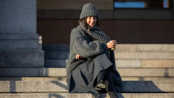 COPENHAGEN, DENMARK - FEBRUARY 01: Benthe Liem sitting drinking coffee wears grey beanie, knit, scarf, skirt, black Prada bag outside Marimekko during the Copenhagen Fashion Week AW24 on February 01, 2024 in Copenhagen, Denmark. (Photo by Christian Vierig/Getty Images)