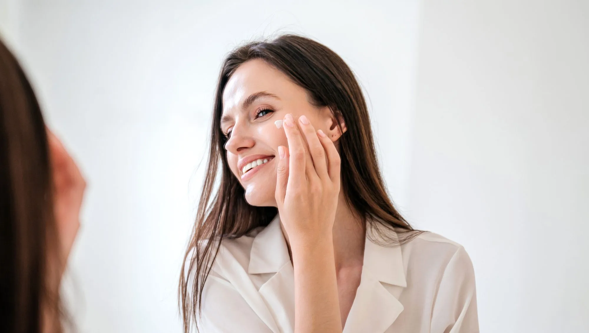 Healthy skin and everyday skincare routine concepts. Portrait of happy female apply anti aging moisturizing cosmetic cream on face, smiling, looking at bathroom mirror