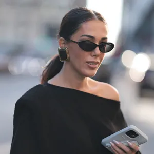 Olga Sokolenko seen wearing black sunglasses, Saint Laurent large gold / black square earrings, Say No More black off-shoulder asymmetrical oversized cotton sweater and Rhode grey silicone lip phone case, during the New York Fashion Week, on September 09, 2024 in New York City.