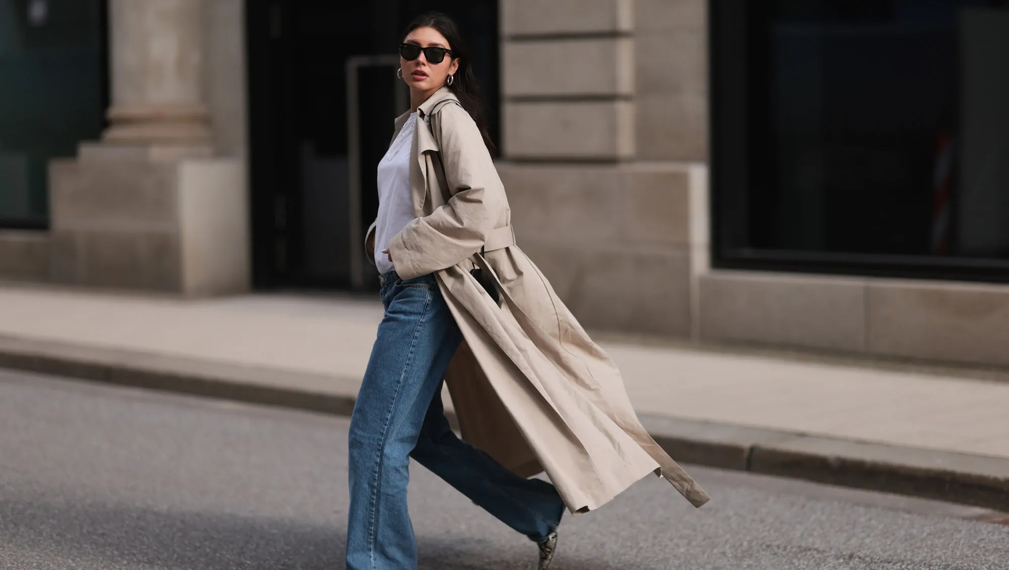 Milena Karl seen wearing Ray-Ban black Wayfarer sunglasses, silver earrings, Hermès silver chain / necklace, The Row beige oversized long coat, NA-KD blue denim wide leg jeans / pants, COS white cotton basic shirt, Alaia black leather heart shaped crossbody bag and Ganni beige snake pattern leather heeled boots, on February 23, 2024 in Hamburg, Germany.