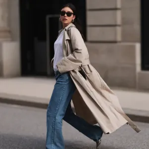 Milena Karl seen wearing Ray-Ban black Wayfarer sunglasses, silver earrings, Hermès silver chain / necklace, The Row beige oversized long coat, NA-KD blue denim wide leg jeans / pants, COS white cotton basic shirt, Alaia black leather heart shaped crossbody bag and Ganni beige snake pattern leather heeled boots, on February 23, 2024 in Hamburg, Germany.