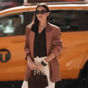 Yana Echko seen wearing YSL brown sunglasses, Bottega Veneta brown leather earrings, white pearl necklace, The Frankie Shop brown pinstripe vest, Express light brown corduroy blazer jacket, Reformation cream white maxi silk long skirt, MARGE SHERWOOD brown suede leather small bag, Kenneth Jay Lane gold ring, cream white / brown bangle, outside the Bach Mai show, during the New York Fashion Week, on September 08, 2024 in New York City.