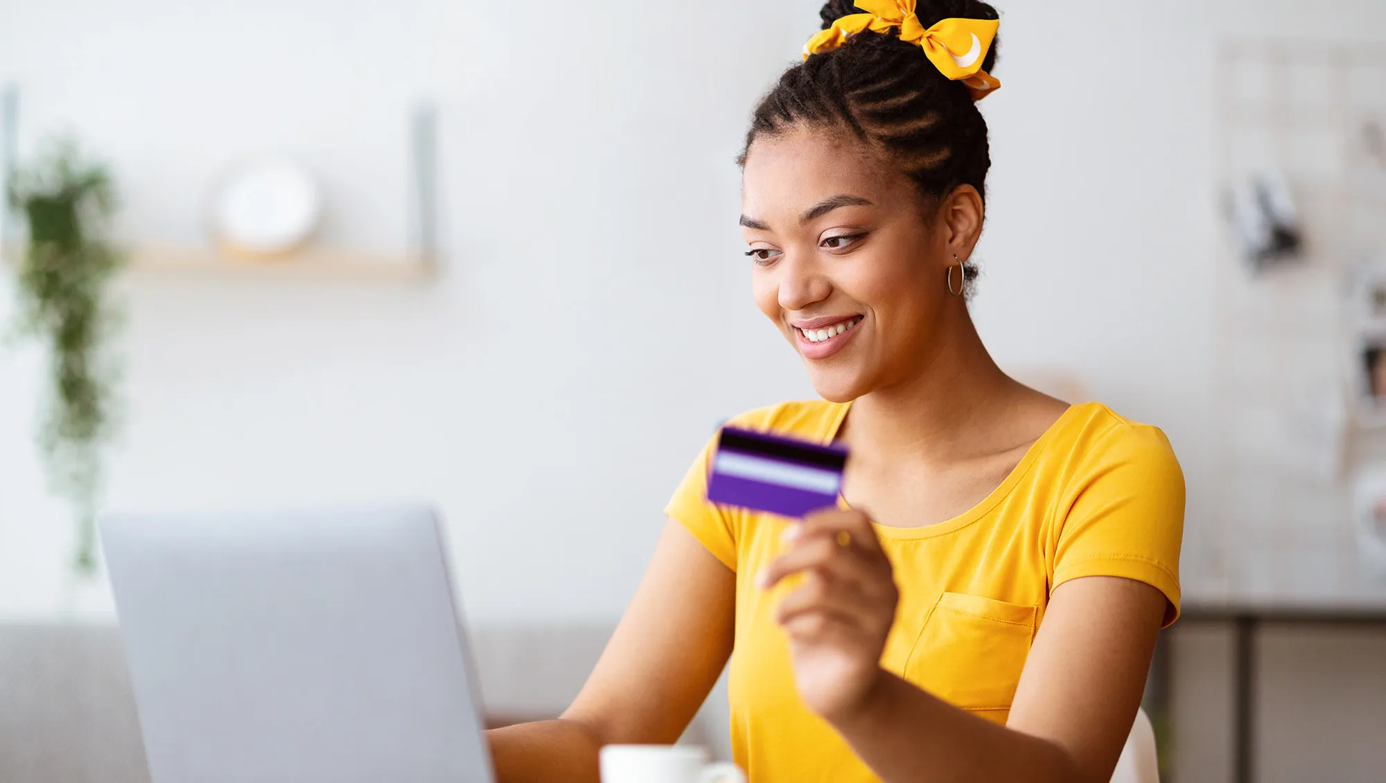 Online Shopping Concept. Portrait of smiling african american woman holding credit card in hand and using laptop, sitting at desk, typing on keyboard, blurred background, selective focus. Ecommerce