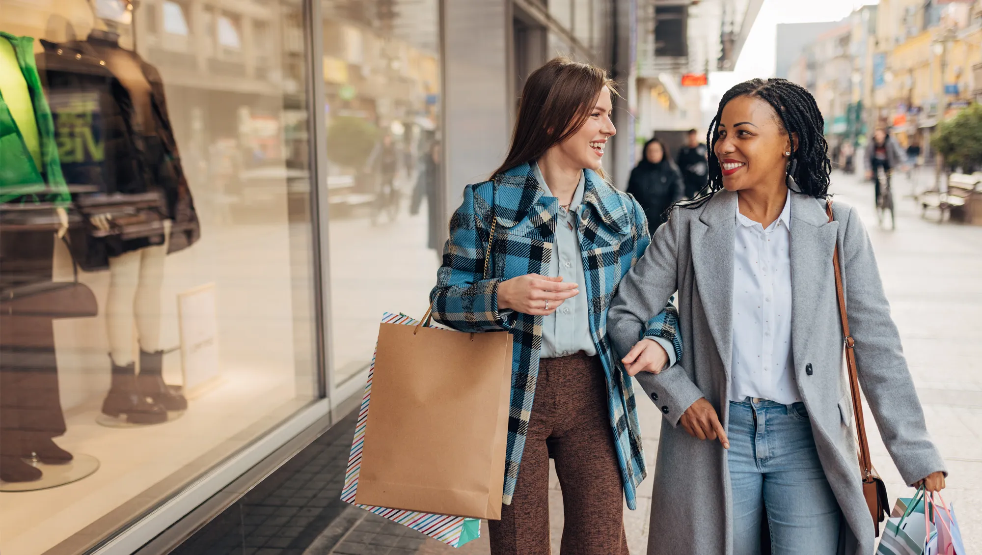 Two cheerful women in coats are walking around town with shopping bags after shopping