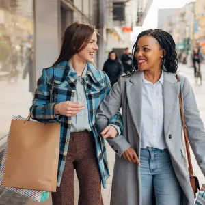 Two cheerful women in coats are walking around town with shopping bags after shopping
