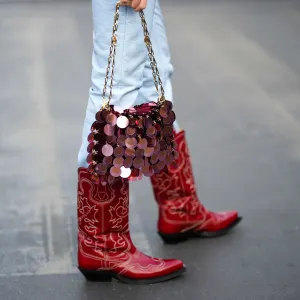 PARIS, FRANCE - MARCH 01: A guest wears pale blue shiny leather skinny pants, a burgundy coins handbag from Paco Rabanne, red shiny leather with embroidered white pattern pointed block heels knees boots , outside Cecilie Bahnsen, during Paris Fashion Week - Womenswear Fall Winter 2023 2024, on March 01, 2023 in Paris, France. (Photo by Edward Berthelot/Getty Images)