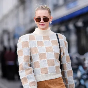 A guest wears sunglasses, a white and beige checkered / checked pattern printed turtleneck ribbed wool pullover with shoulder pads, a beige / brown suede mini skirt , outside Mark Kenly Domino Tan, during the Copenhagen Fashion Week AW24 on February 01, 2024 in Copenhagen, Denmark.