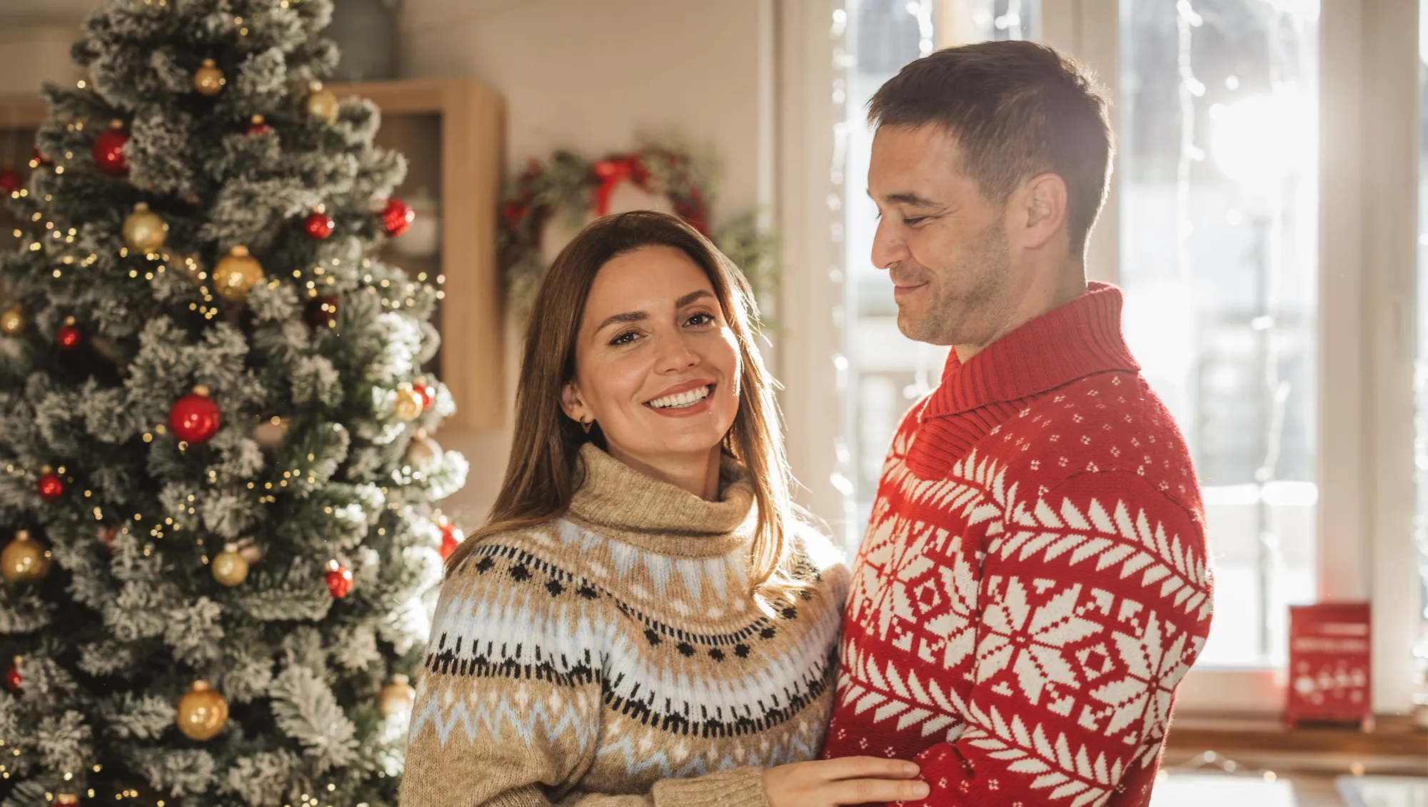 Young couple hugging in front of Christmas tree at home.