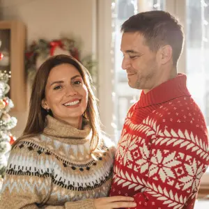 Young couple hugging in front of Christmas tree at home.