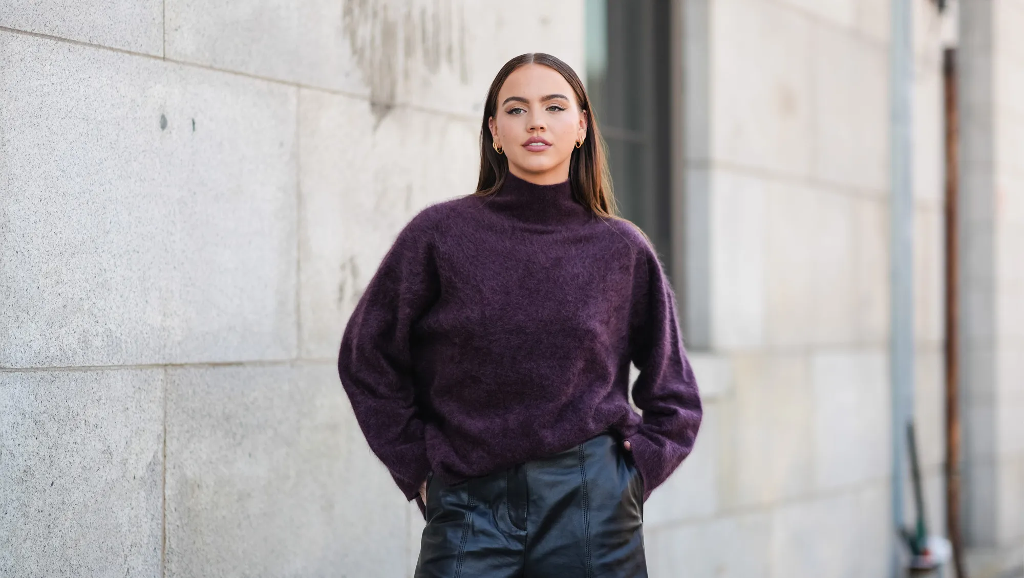 A guest wears dark purple oversized turtleneck sweater, shiny black leather shorts, outside Cos, during the New York Fashion week Spring/Summer 2025 on September 10, 2024 in New York, New York.
