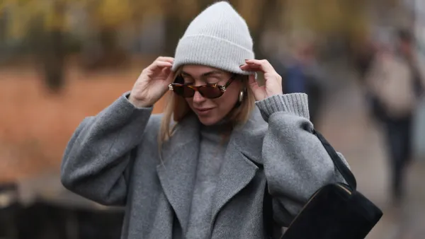 BERLIN, GERMANY - NOVEMBER 14: Sonia Lyson is seen wearing a light grey knit beanie from Le Bonnet; chunky silver hoop earrings; oval sunglasses with Havana frame and silver details from Givenchy; a calf-length grey wool coat with notch lapels from & Other Stories; a light grey knit sweater with ribbed turtleneck and cuffs from Sézane; and a rectangular black suede handbag from Elleme on November 14, 2024 in Berlin, Germany. (Photo by Jeremy Moeller/Getty Images)
