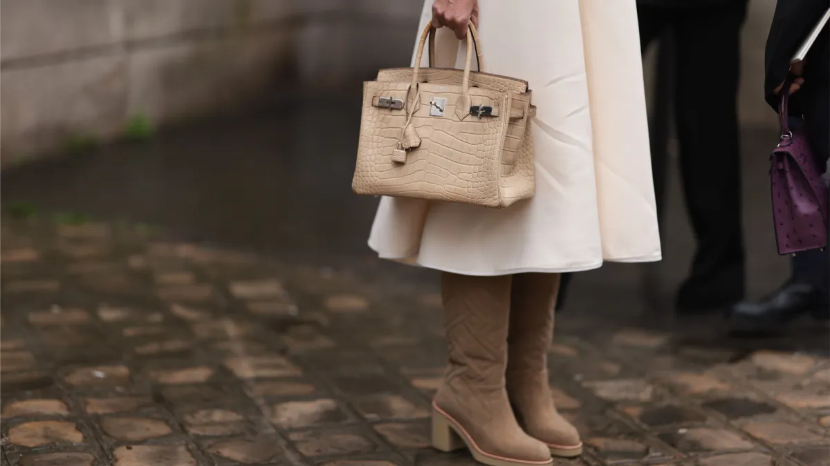 Fashion Week Guest seen wearing Hermes birkin bag creme crocodile exotic leather, Cartier panthere silver watch, white long skirt, brown boots outside Hermes show, during the Womenswear Fall/Winter 2024/2025 as part of Paris Fashion Week on March 02, 2024 in Paris, France.