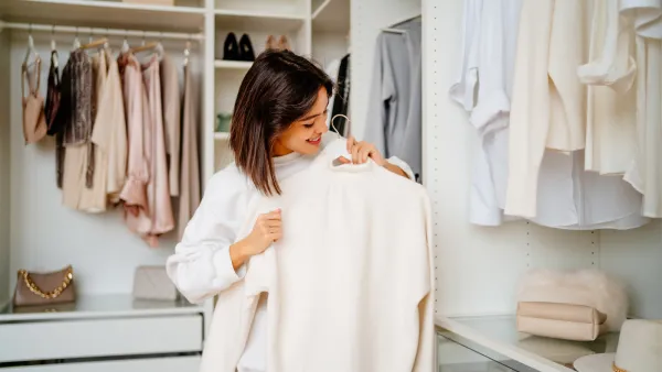 Dark haired woman in white sweater holding jumper rack in the closet room