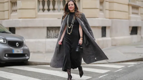 Alba Garavito Torre wears a black Giulia Mastini gathered dress, a grey long coat, long pearls Sempiterno necklace, black lace tights, a black leather mini kelly Hermes bag, black satin Gucci high heels, during a street style fashion photo session, on December 18, 2024 in Paris, France