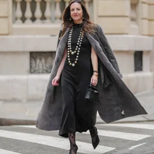 Alba Garavito Torre wears a black Giulia Mastini gathered dress, a grey long coat, long pearls Sempiterno necklace, black lace tights, a black leather mini kelly Hermes bag, black satin Gucci high heels, during a street style fashion photo session, on December 18, 2024 in Paris, France