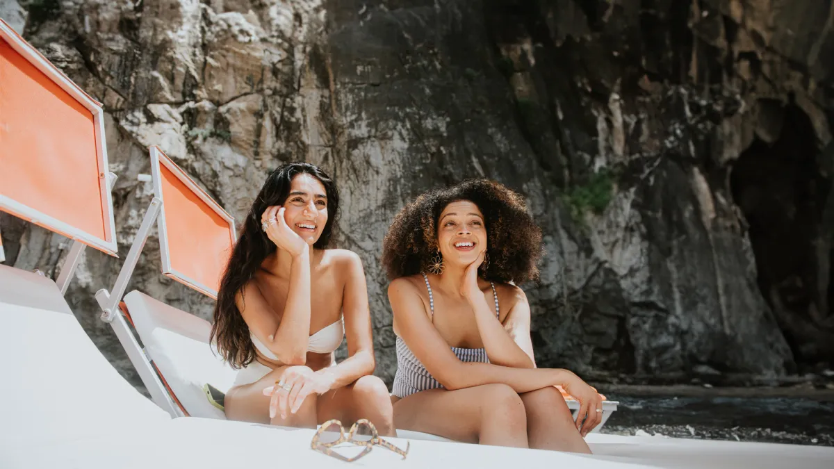 Female friends laugh as they apply suncream together