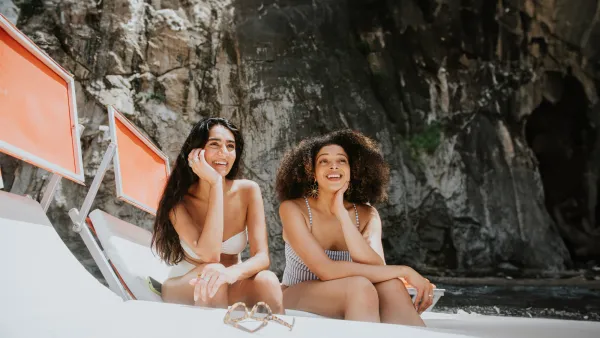 Female friends laugh as they apply suncream together