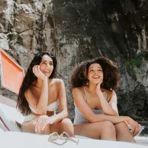 Female friends laugh as they apply suncream together