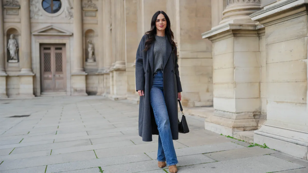 Allison Cardoso wears a grey Uniqlo pullover, a grey Ikks coat, a black leather bag, a blue denim Levis jeans / pants, brown suede Potamy boots high heels, during a street style fashion photo session, on December 04, 2024 in Paris, France.