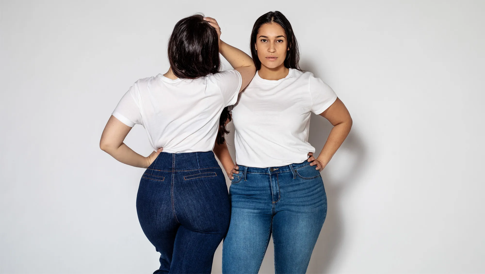 Portrait of two plus size female standing in opposite directions on white background. Women wearing white t-shirt and blue denim jeans.