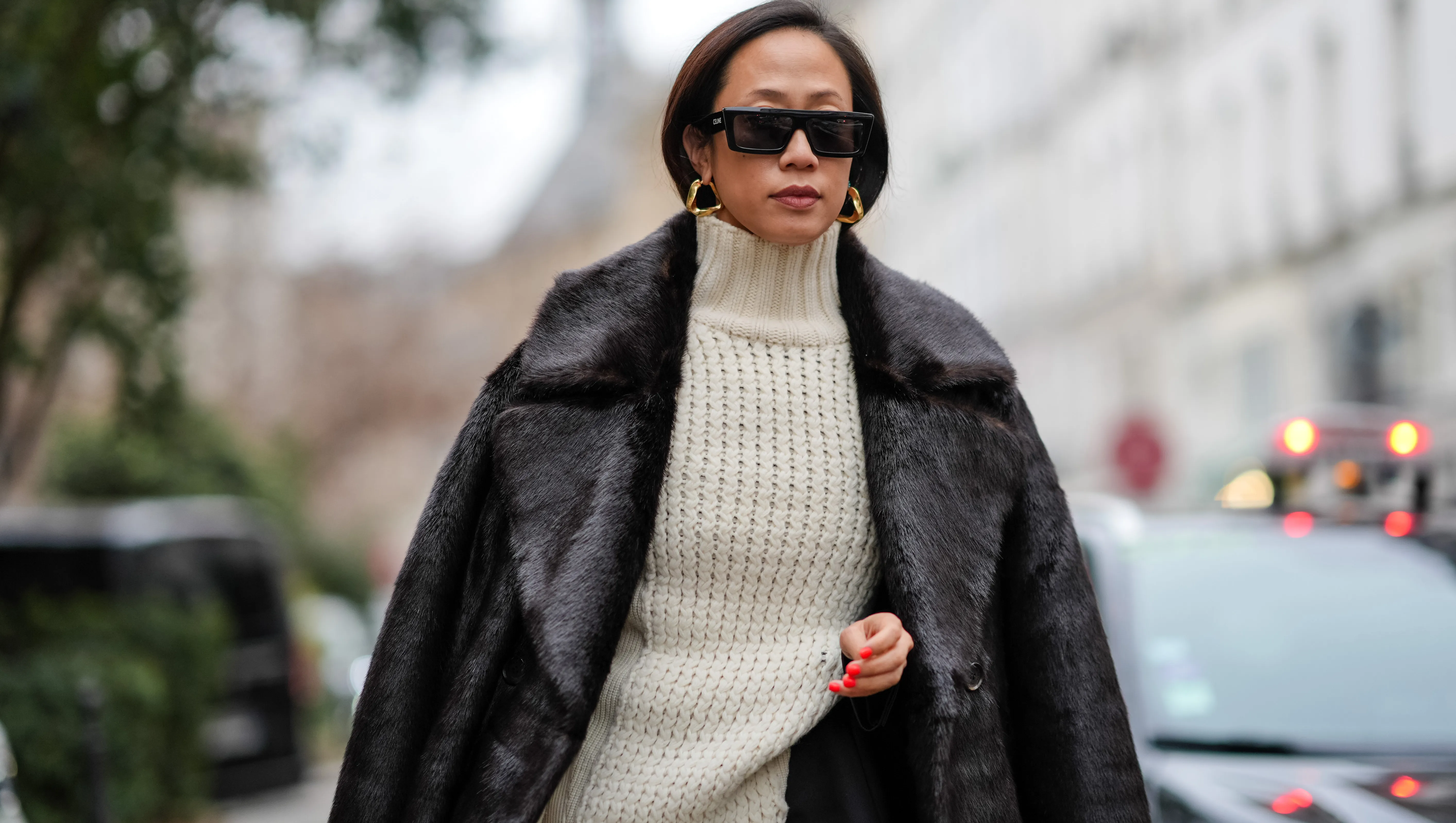 PARIS, FRANCE - JANUARY 21: A guest wears sunglasses, earrings, a white ribbed wool long pullover worn as a dress, a black fluffy long coat, outside Sacai, during the Menswear Fall/Winter 2024/2025 as part of Paris Fashion Week on January 21, 2024 in Paris, France. (Photo by Edward Berthelot/Getty Images)