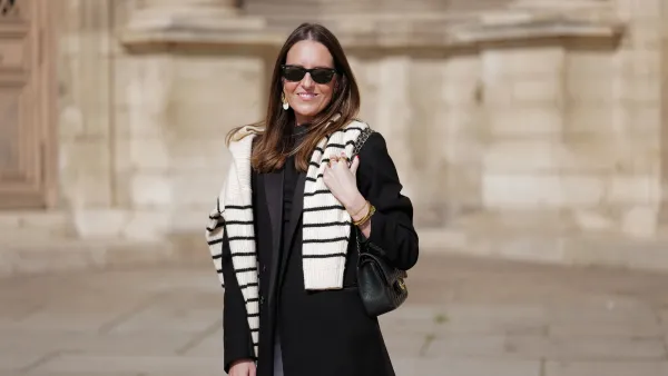 Alba Garavito Torre wears black sunglasses from Ray Ban, gold and white pendant large earrings, a black t-shirt, a white with black small striped print pattern wool pullover from Massimo Dutti, a black shiny grained leather Timeless shoulder bag from Chanel, a black oversized blazer jacket from Munthe, white skinny denim pants from Zara, during a street style fashion photo session, on April 29, 2023 in Paris, France.