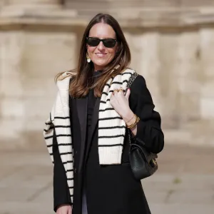 Alba Garavito Torre wears black sunglasses from Ray Ban, gold and white pendant large earrings, a black t-shirt, a white with black small striped print pattern wool pullover from Massimo Dutti, a black shiny grained leather Timeless shoulder bag from Chanel, a black oversized blazer jacket from Munthe, white skinny denim pants from Zara, during a street style fashion photo session, on April 29, 2023 in Paris, France.