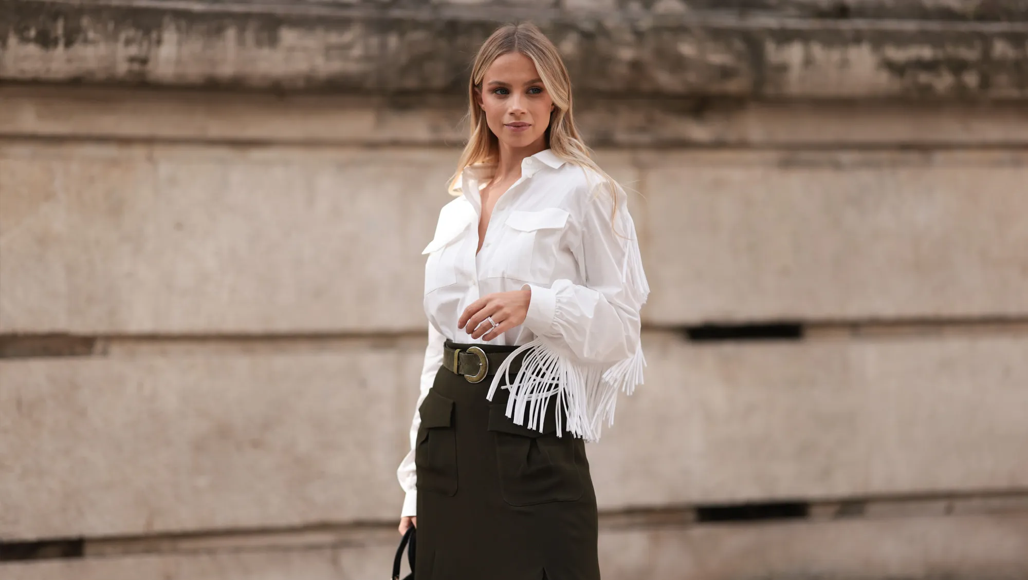 A Fashion Week guest is seen wearing a white shirt with fringes along the sleeves, tucked into an olive midi skirt with pockets at the front, paired with an olive suede belt featuring a round buckle, a silver structured ring, and the rectangular “Lady Dior“ bag in black quilted leather with gold details from Dior before the Elie Saab Womenswear Spring/Summer 2025 Show as part of Paris Fashion Week on September 28, 2024 in Paris, France