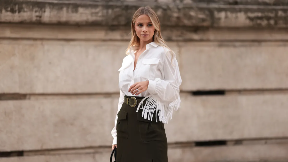 A Fashion Week guest is seen wearing a white shirt with fringes along the sleeves, tucked into an olive midi skirt with pockets at the front, paired with an olive suede belt featuring a round buckle, a silver structured ring, and the rectangular “Lady Dior“ bag in black quilted leather with gold details from Dior before the Elie Saab Womenswear Spring/Summer 2025 Show as part of Paris Fashion Week on September 28, 2024 in Paris, France