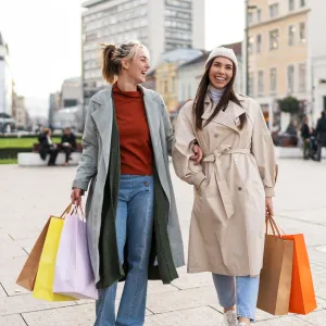 Two female friends holding shopping bags and smiling while walking in the city