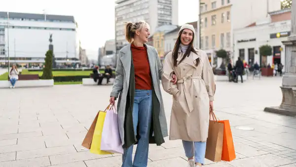 Two female friends holding shopping bags and smiling while walking in the city